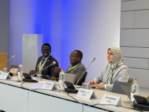 Three people sit in front of microphones at a board meeting.
