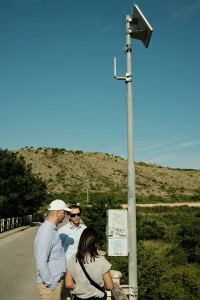 Group of three people looking at a weather station on a bridge.