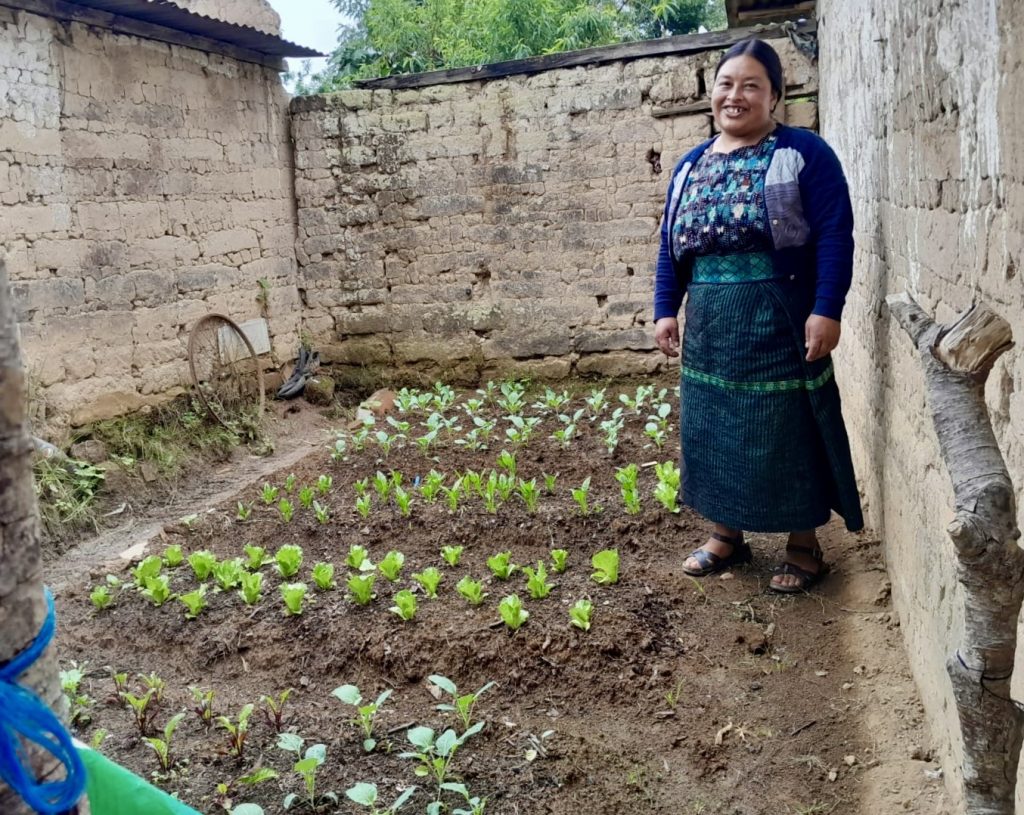 A woman stands in her garden, vegetables sprouting from the ground
